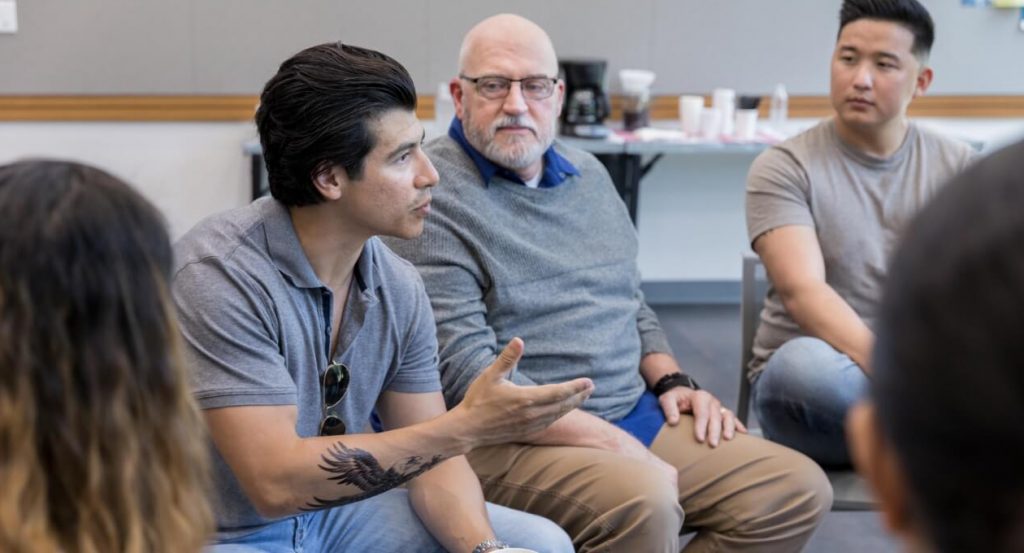 Man talking to a group of people sitting in a circle
